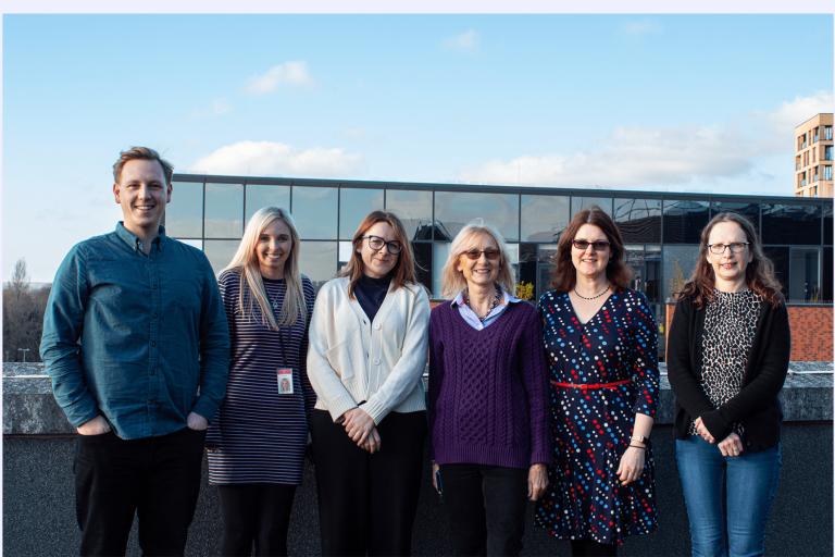 Team members standing together in front of a wall with the sun shining