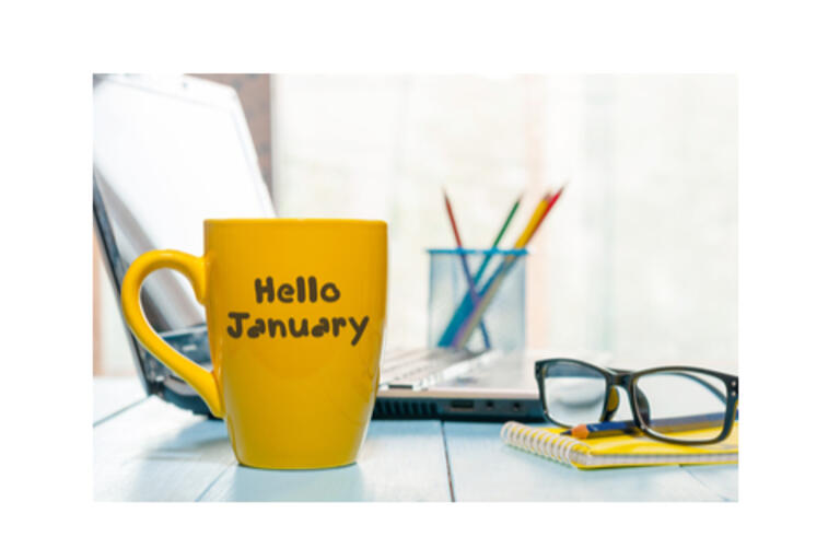 Yellow mug saying 'Hello January' with some pens in a pot and spectacles