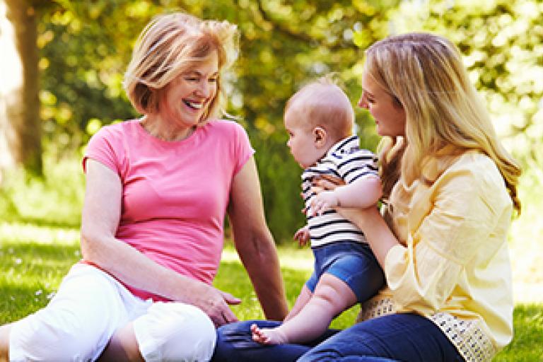 Two women sitting on a picnic blanket with a baby, one woman is older and one younger