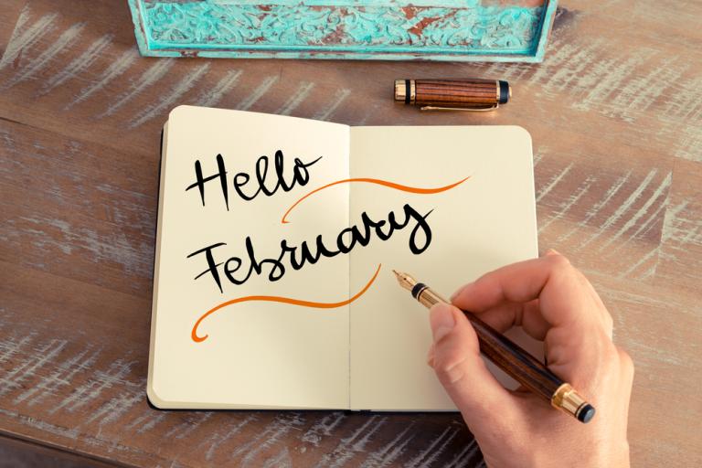 Hand writing 'hello February' into a notebook