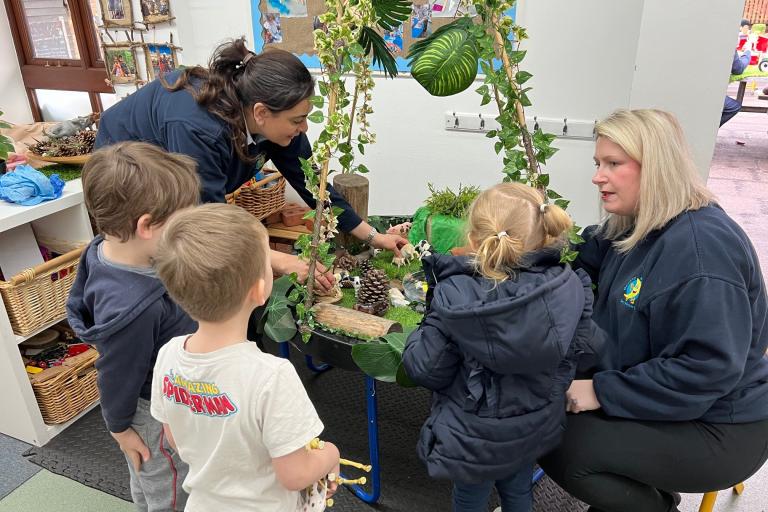 Staff and children sitting around a desk at Banana Moon nursery in Billericay