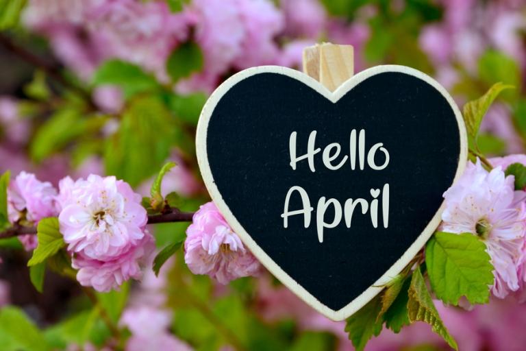 Hello April written in a heart shaped chalk board, surrounded by purple spring flowers