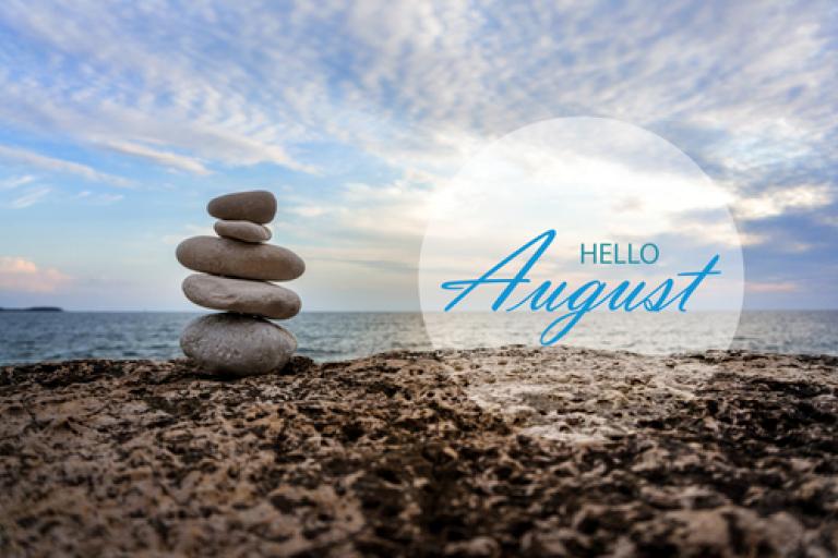 Words hello August set against a backdrop of a beach with a pile of stones