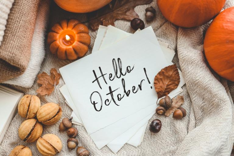 The words hello October on a white piece of paper, sitting on top of some hessian and surrounded by pumpkins, nuts and seeds