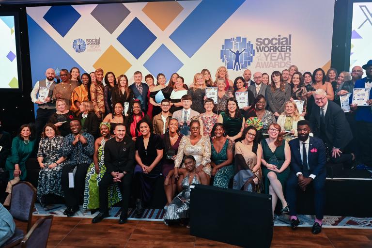 Group of winners on a stage, all sitting in front of a white backdrop with the words Social Worker of the Year Awards