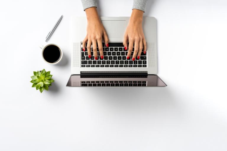 Picture showing laptop with hands typing at it, alongside a cup of coffee