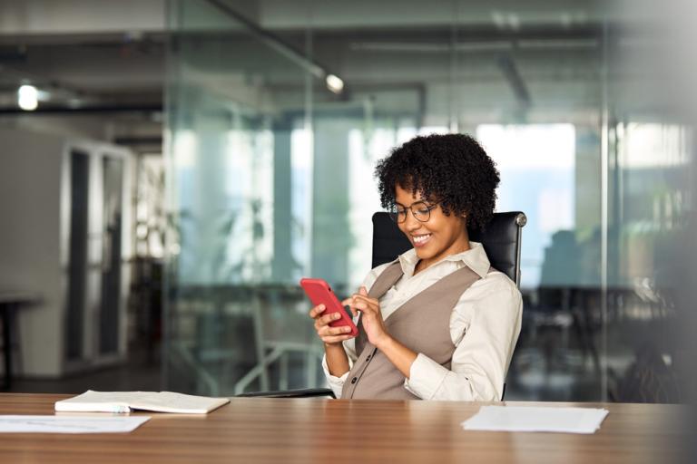 Woman in an office, scrolling on a phone and smiling