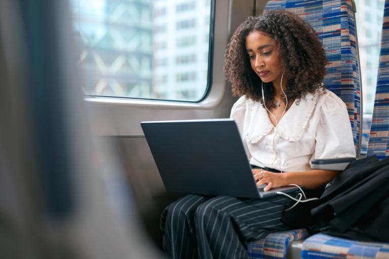 Woman on laptop on train with headphones in