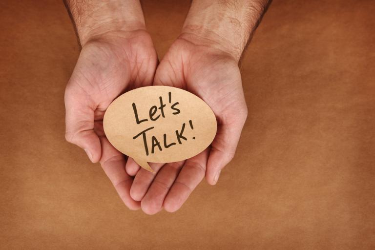 Hands held out holding a piece of wood with the words Let's talk on it