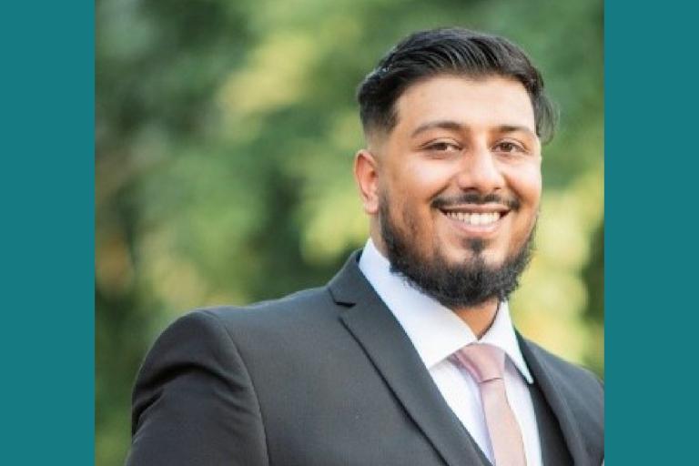 Mohammed in a suit standing outside in front of some trees