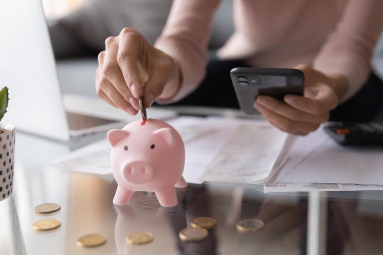 Woman holding a calculator and putting coins into a piggy bank