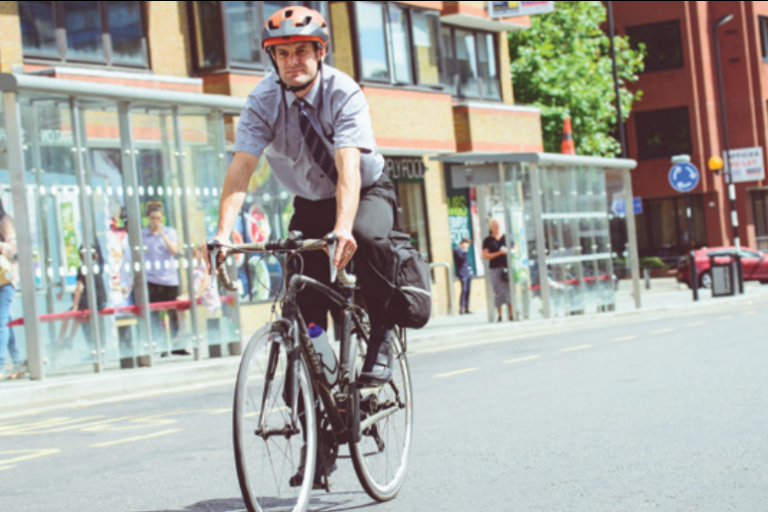 Man on bike riding through town, wearing cycle helmet shirt and trousers