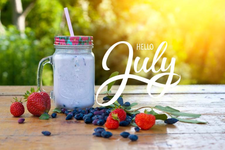 Words hello July with a mug of smoothie, surrounded by blueberries and strwaberries