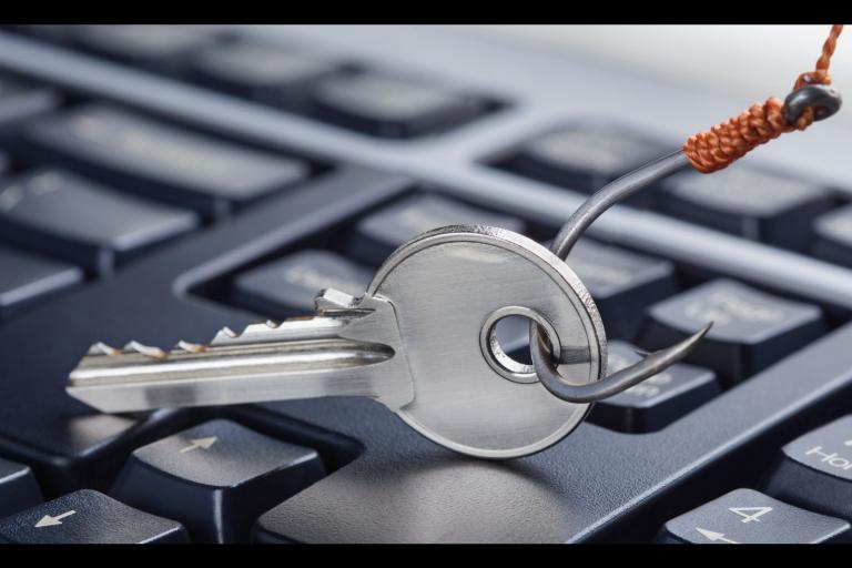 Computer keyboard shown with a silver fishing hook being dangled over it