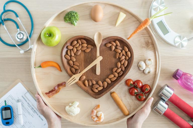 A clock - shaped image with a heart shape inside it, with lots of healthy nuts and fruits. Surrounded by a stethoscope, scales, weights for exercise