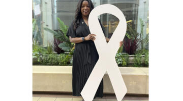 Sabrina Robinson in the atrium at County Hall holding a giant white ribbon symbol