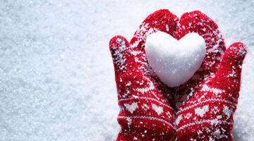 Heart made of snow in two gloved hands