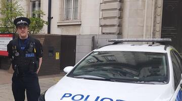 Johnathon in police uniform, next to a police car, outside County Hall