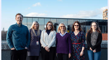 Team members standing together in front of a wall with the sun shining