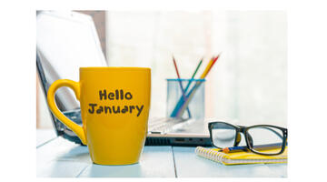 Yellow mug saying 'Hello January' with some pens in a pot and spectacles