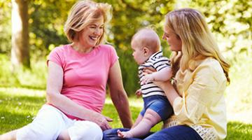Two women sitting on a picnic blanket with a baby, one woman is older and one younger