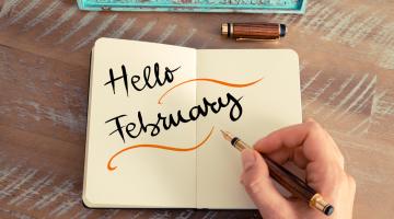 Hand writing 'hello February' into a notebook