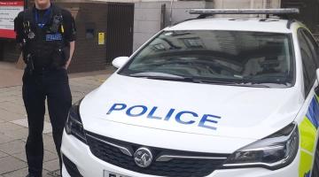 Johnathon Cuthbertson in police uniform beside a police car outside County Hall