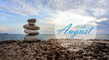 Words hello August set against a backdrop of a beach with a pile of stones