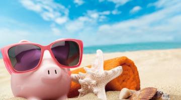 Piggybank in sunglasses relaxing on a beach next to a starfish