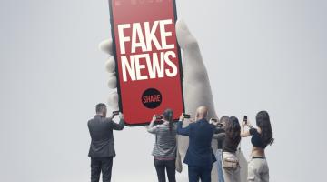 A giant mobile phone with 'fake news.share' written on it. Surrounded by a group of much smaller people taking photos of it with their mobile phones