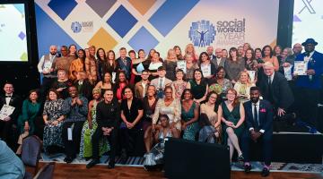 Group of winners on a stage, all sitting in front of a white backdrop with the words Social Worker of the Year Awards