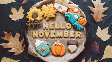 Log stump surrounded by Autumn leaves with the words Hello November