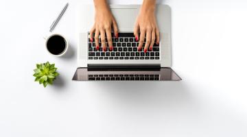 Picture showing laptop with hands typing at it, alongside a cup of coffee