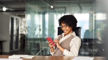 Woman in an office, scrolling on a phone and smiling