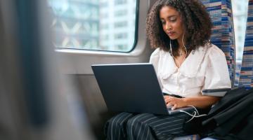 Woman on laptop on train with headphones in