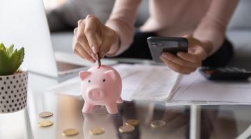 Woman holding a calculator and putting coins into a piggy bank