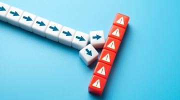 A line of white blocks with arrows on them. The line is disrupted by a series of red blocks with hazard signs on them, going in a different direction