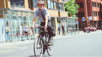 Man on bike riding through town, wearing cycle helmet shirt and trousers