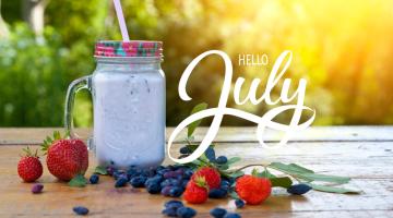 Words hello July with a mug of smoothie, surrounded by blueberries and strwaberries