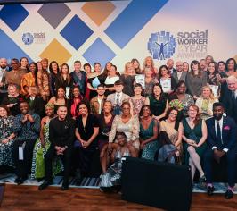 Group of winners on a stage, all sitting in front of a white backdrop with the words Social Worker of the Year Awards