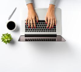 Picture showing laptop with hands typing at it, alongside a cup of coffee