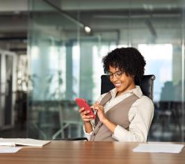 Woman in an office, scrolling on a phone and smiling