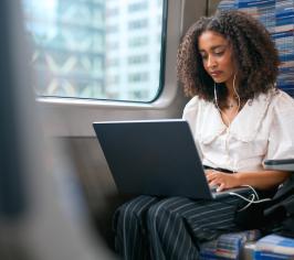 Woman on laptop on train with headphones in