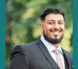 Mohammed in a suit standing outside in front of some trees