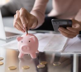 Woman holding a calculator and putting coins into a piggy bank