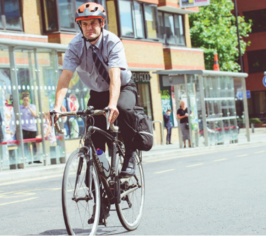 Man on bike riding through town, wearing cycle helmet shirt and trousers