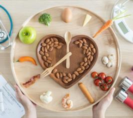 A clock - shaped image with a heart shape inside it, with lots of healthy nuts and fruits. Surrounded by a stethoscope, scales, weights for exercise